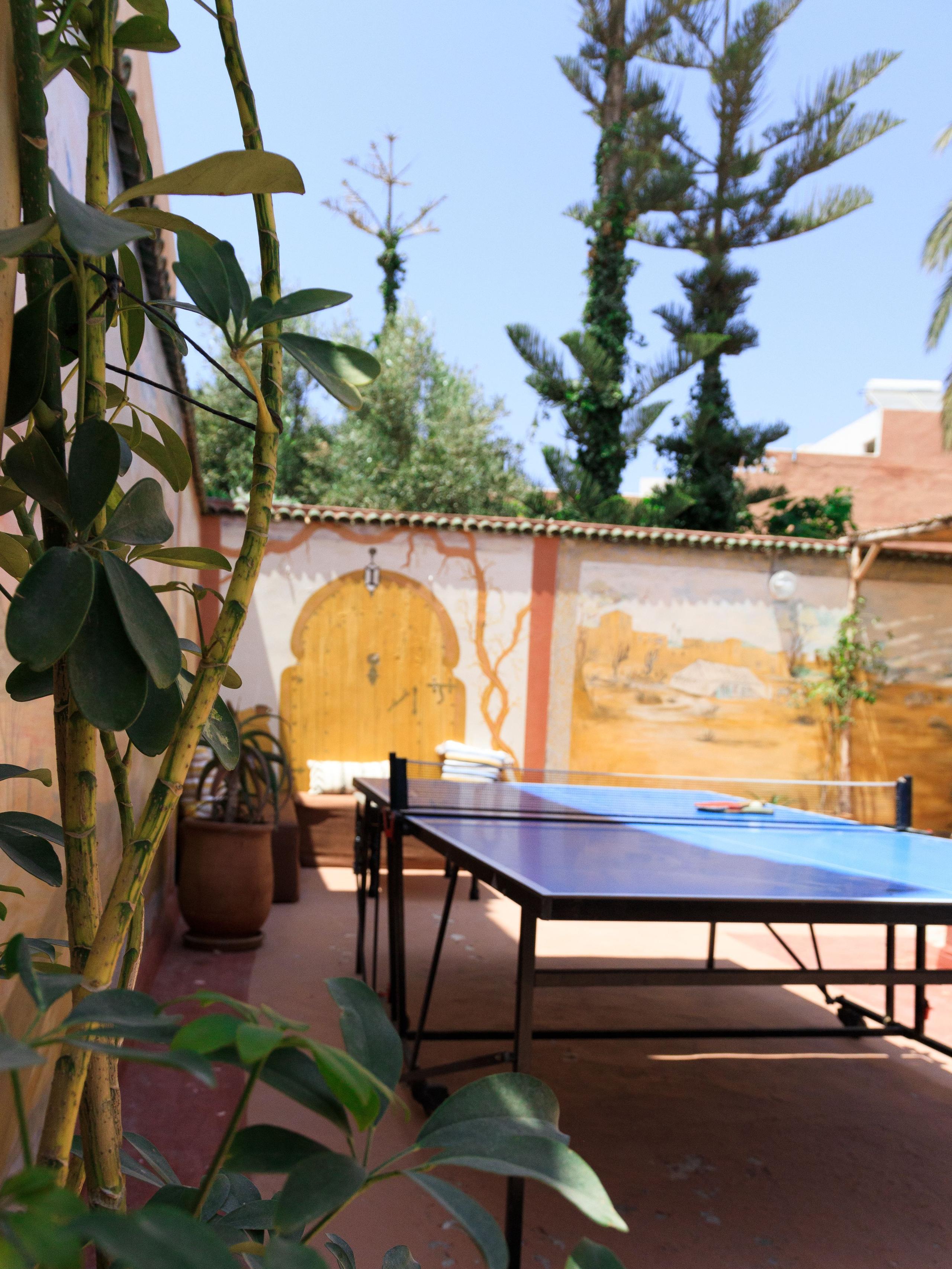 Outdoor garden area with a ping-pong table, plants, and a painted Moroccan mural on the wall