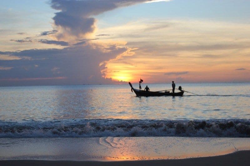 Sunset over the sea at Koh Lanta beach with a traditional longtail boat silhouette