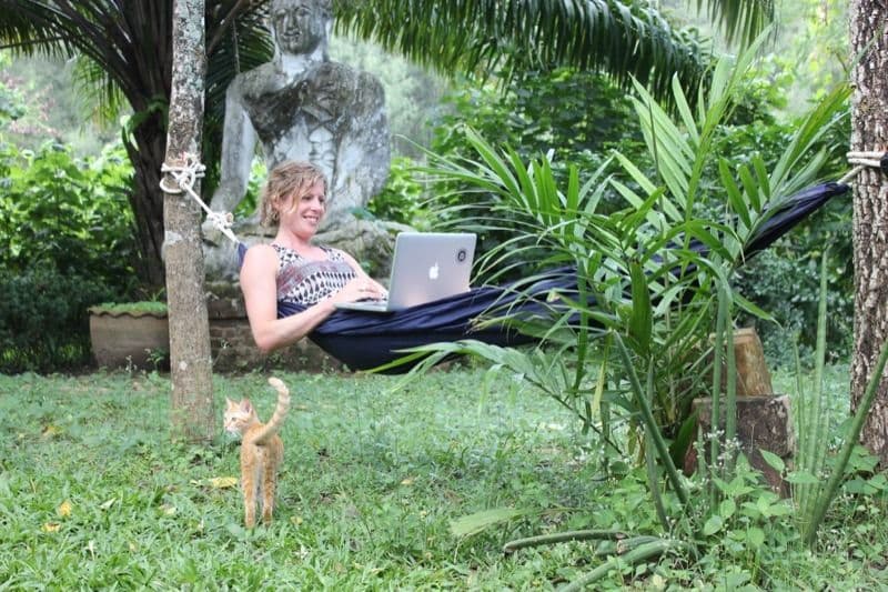 Member relaxing in a hammock with a laptop in the tropical garden, with a cat nearby
