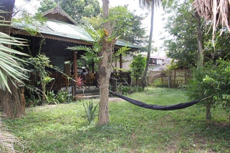 Traditional Thai-style wooden bungalow with green roof surrounded by tropical garden and hammock