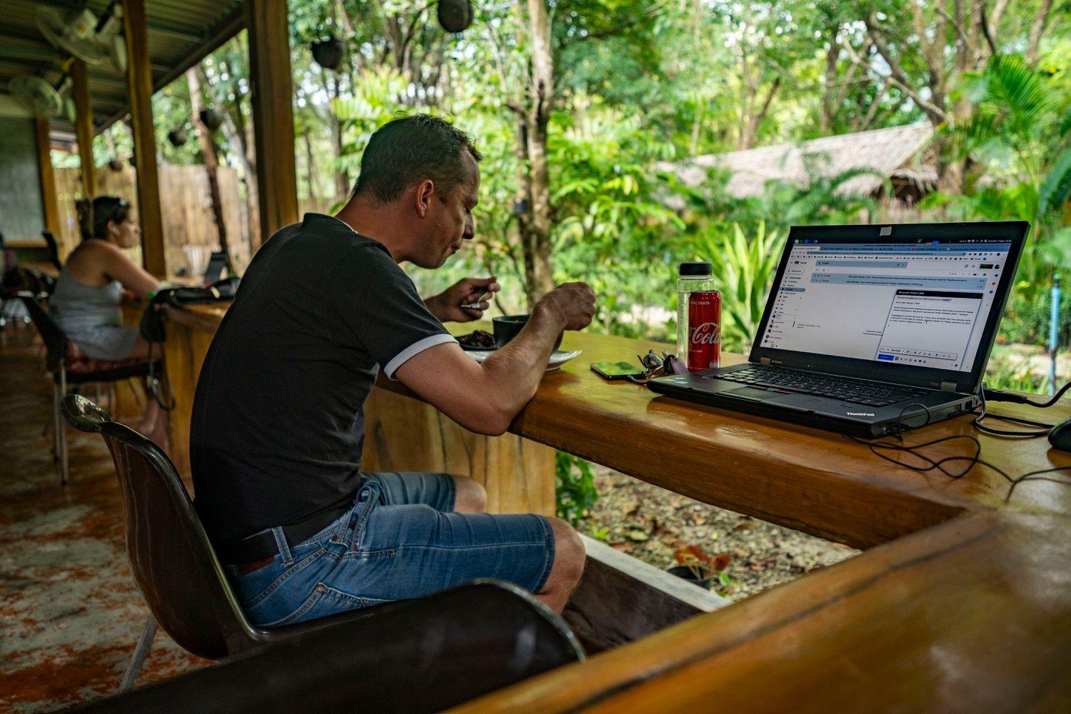 Member working on a laptop at the outdoor deck bar counter overlooking the tropical garden