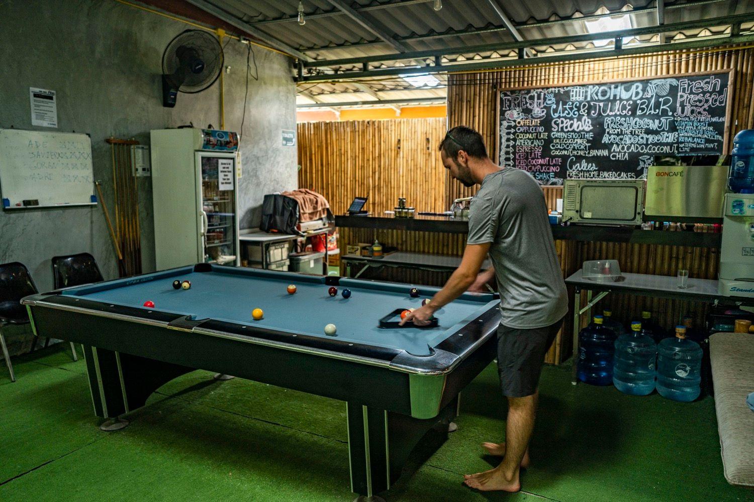 Member playing pool at the pool table with the KoHub cafe and juice bar menu visible in the background