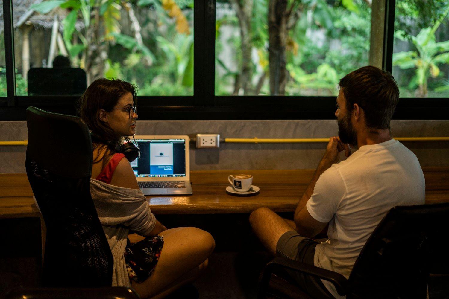 Two members working on laptops at a desk in the indoor coworking area with garden views