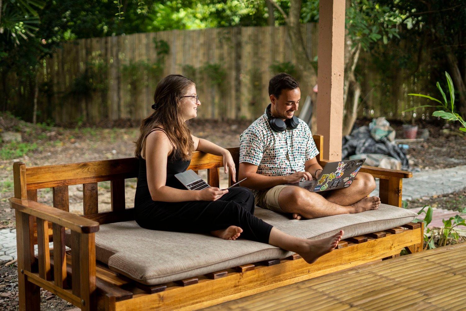 Two members sitting on a wooden bench in an outdoor garden area with laptops