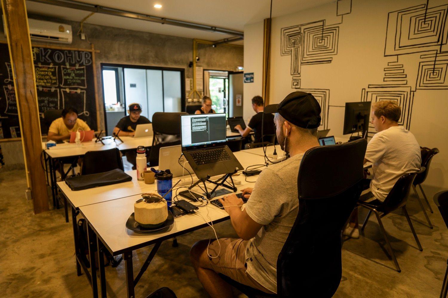 Air-conditioned indoor coworking room with members working on laptops, KoHub signage on wall