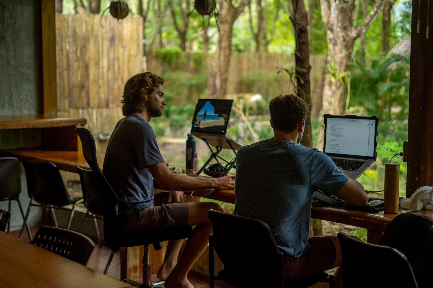 Two members working on laptops at the outdoor deck with garden views