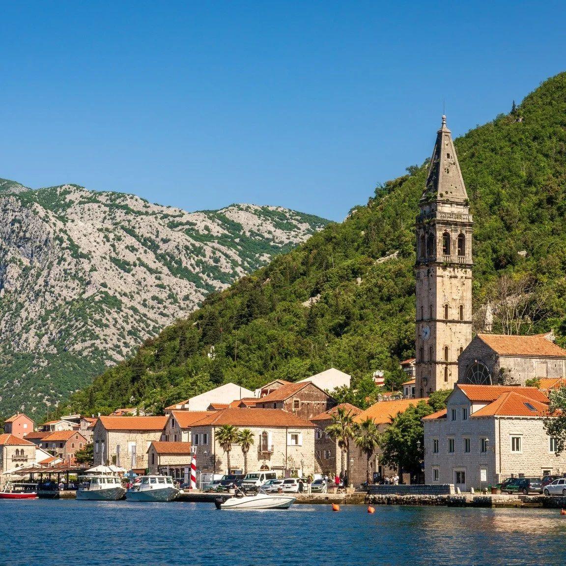 View of Perast town with church bell tower, boats, and mountains in Montenegro