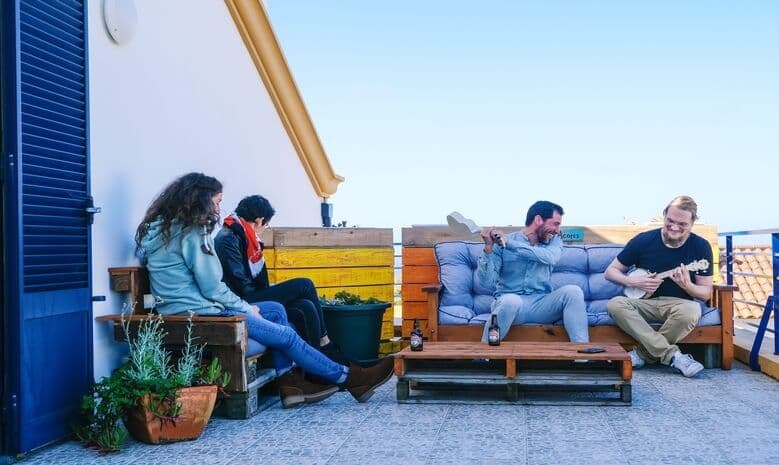 Four residents relaxing on the outdoor terrace with pallet furniture and potted plants
