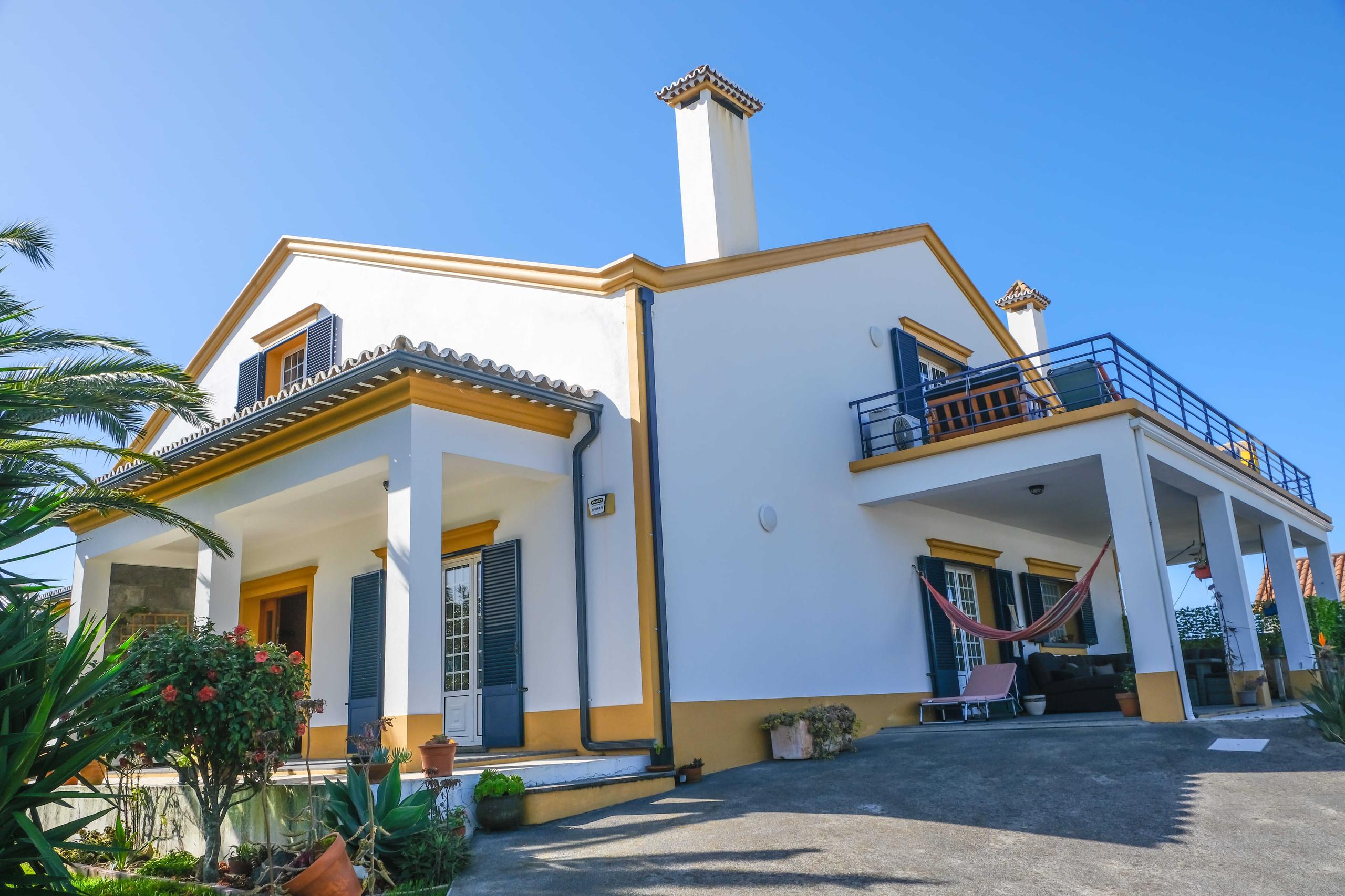 Exterior view of the Lava Coliving house showing the white and yellow facade with a terrace balcony and tropical garden