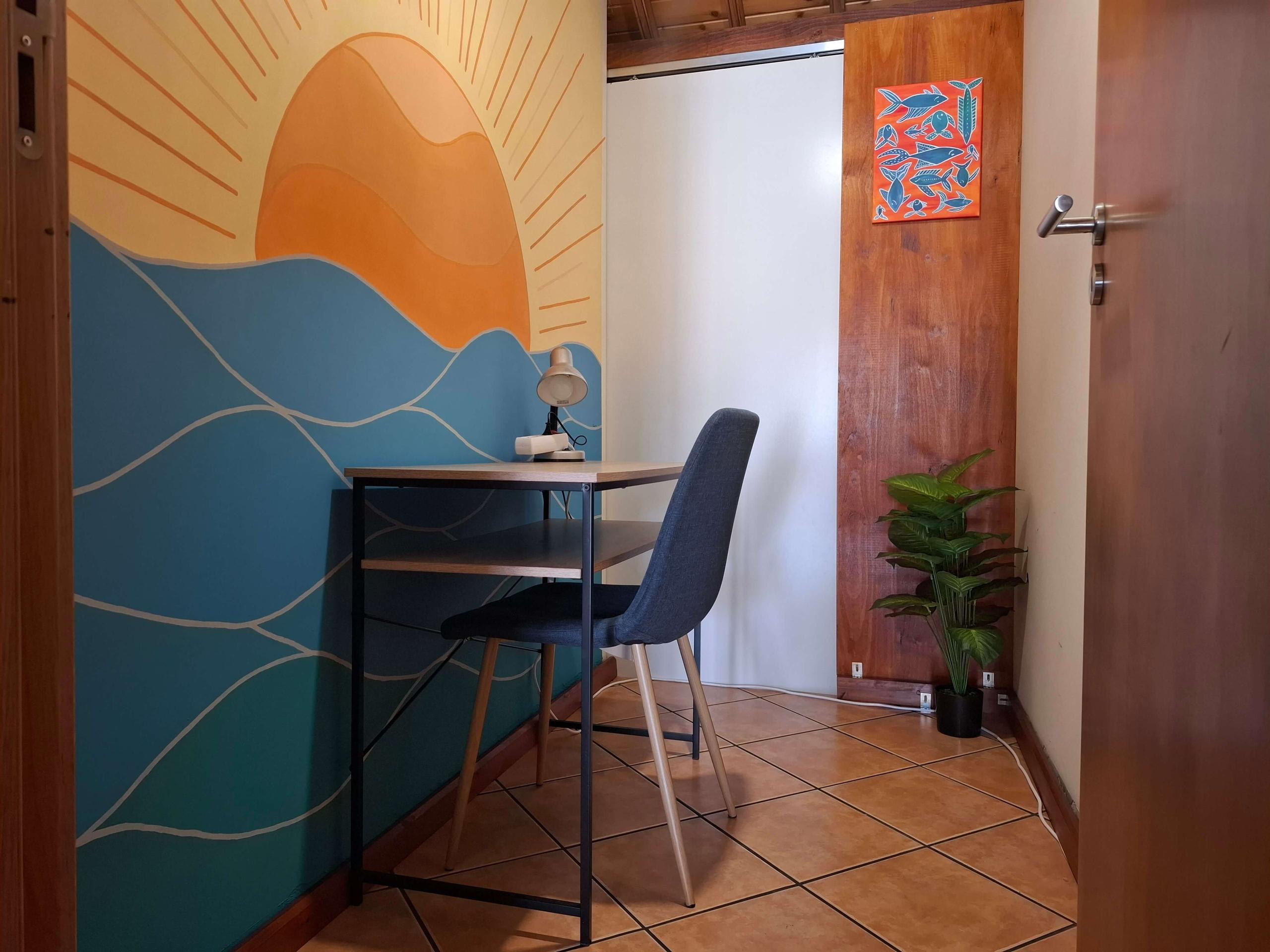 Small private call booth with a desk, chair and a colourful ocean-themed mural on the wall