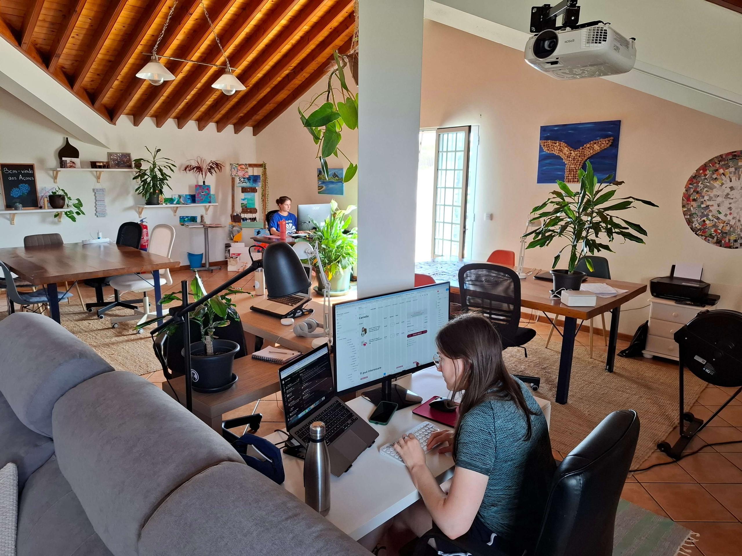 Digital nomads working at desks in the open-plan coworking space with vaulted wooden ceiling and a projector