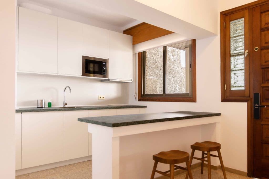 White kitchen with built-in microwave, breakfast bar with stools and window
