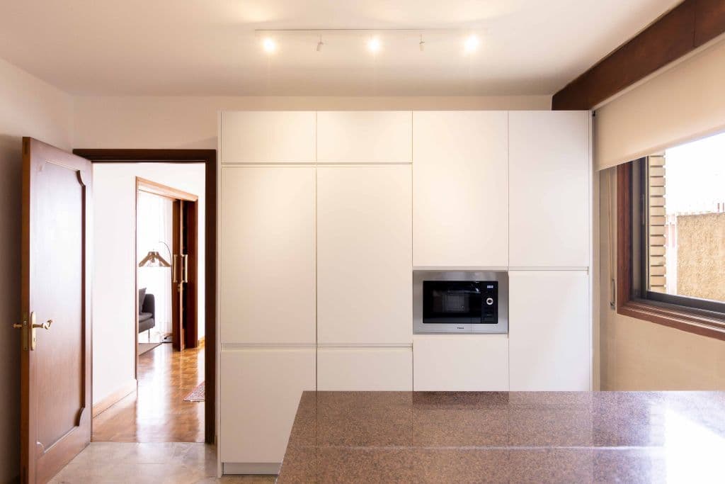 White kitchen with built-in microwave, view through to hallway and living room