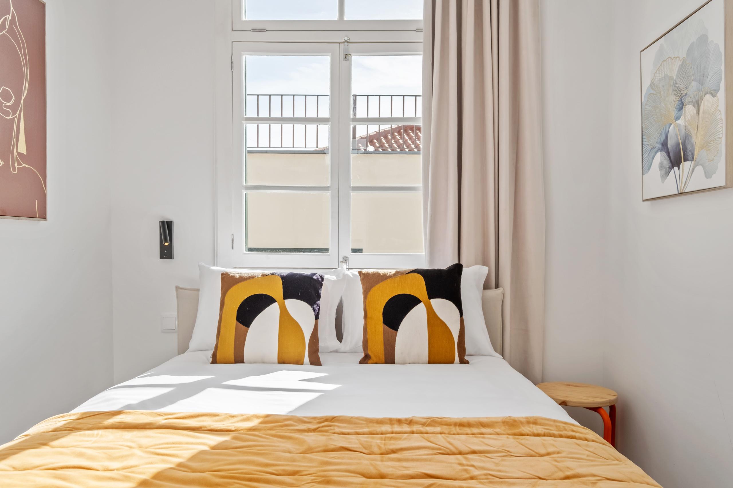 Cozy budget-friendly room with double bed, geometric cushions, artwork, and window