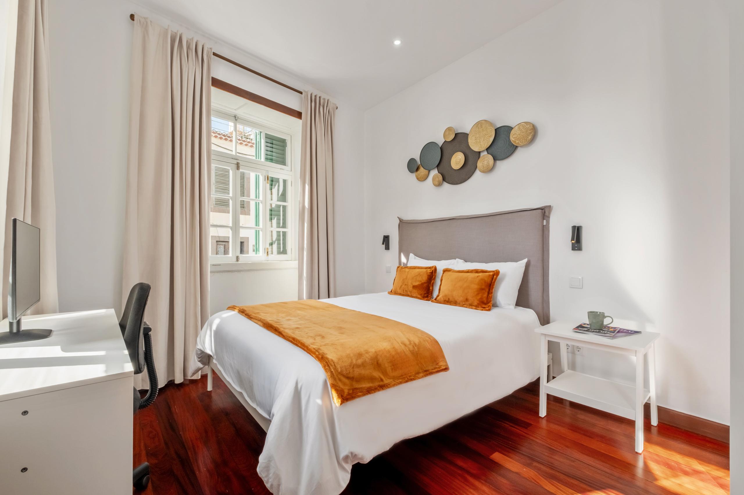 Premium ensuite room with queen bed, orange cushions, desk with monitor, and wooden floors