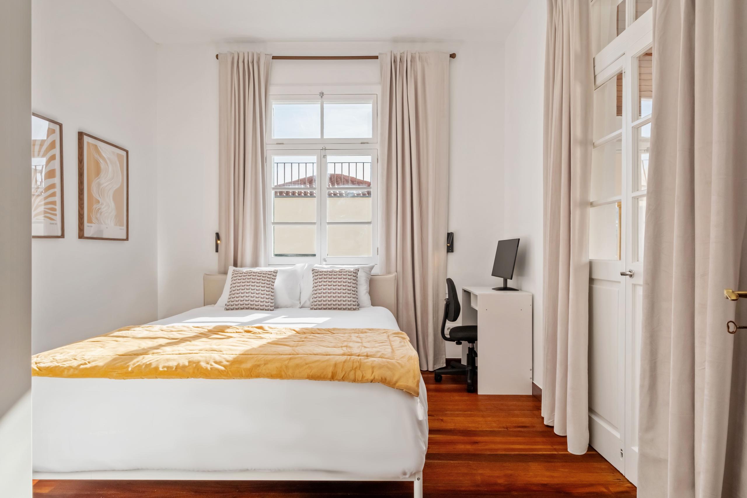 Comfortable room with queen bed, artwork on wall, desk with monitor, and window with curtains