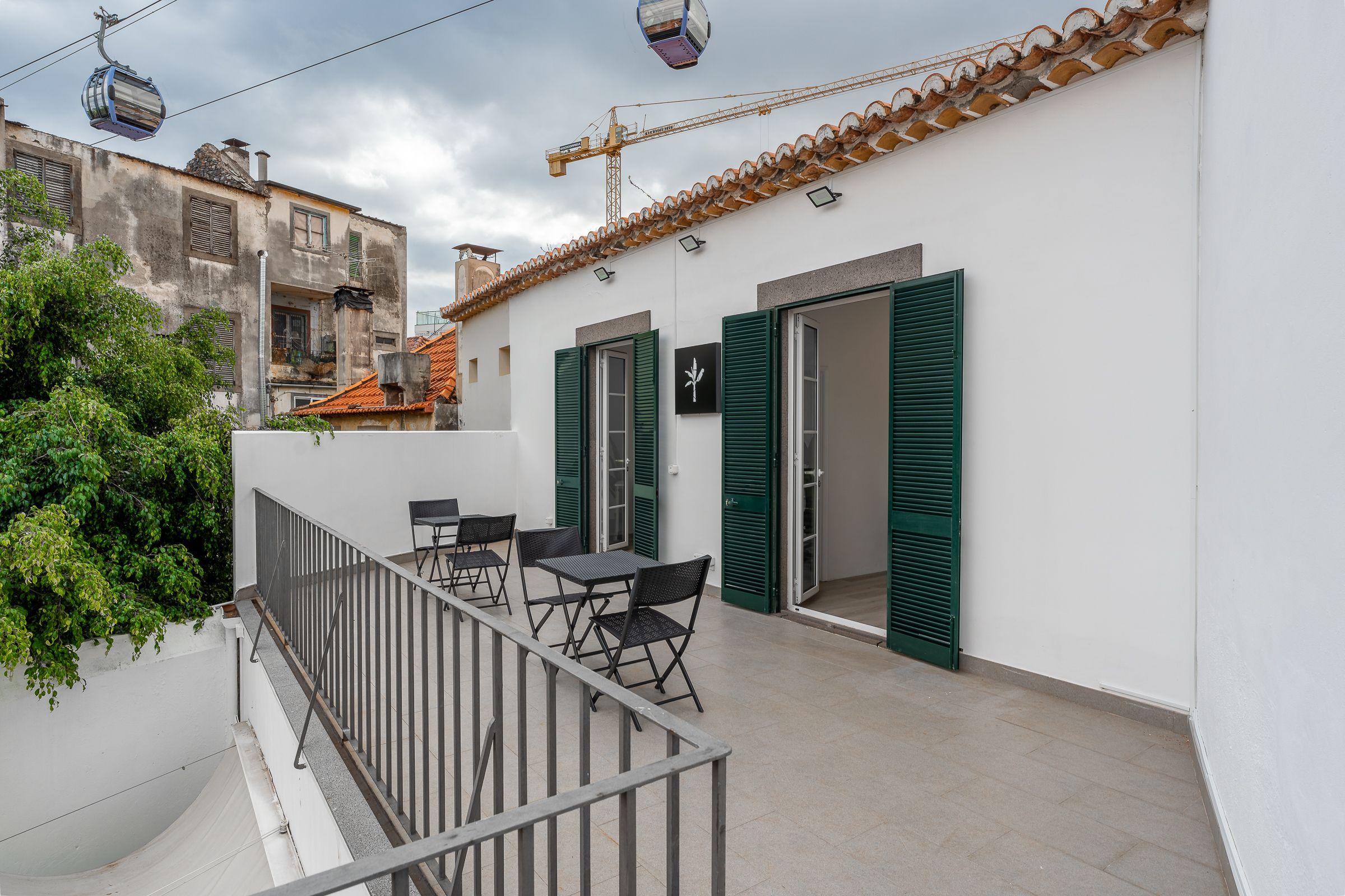Exterior terrace of Madeira Friends Hub with green shuttered doors, cable car visible overhead, and Funchal rooftops