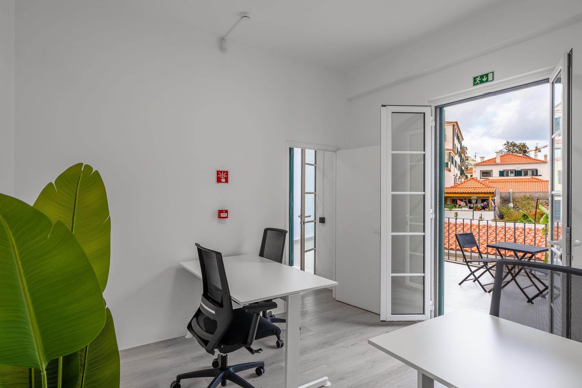 Private work room at Madeira Friends Hub with desk, chairs, and open balcony doors overlooking Funchal rooftops