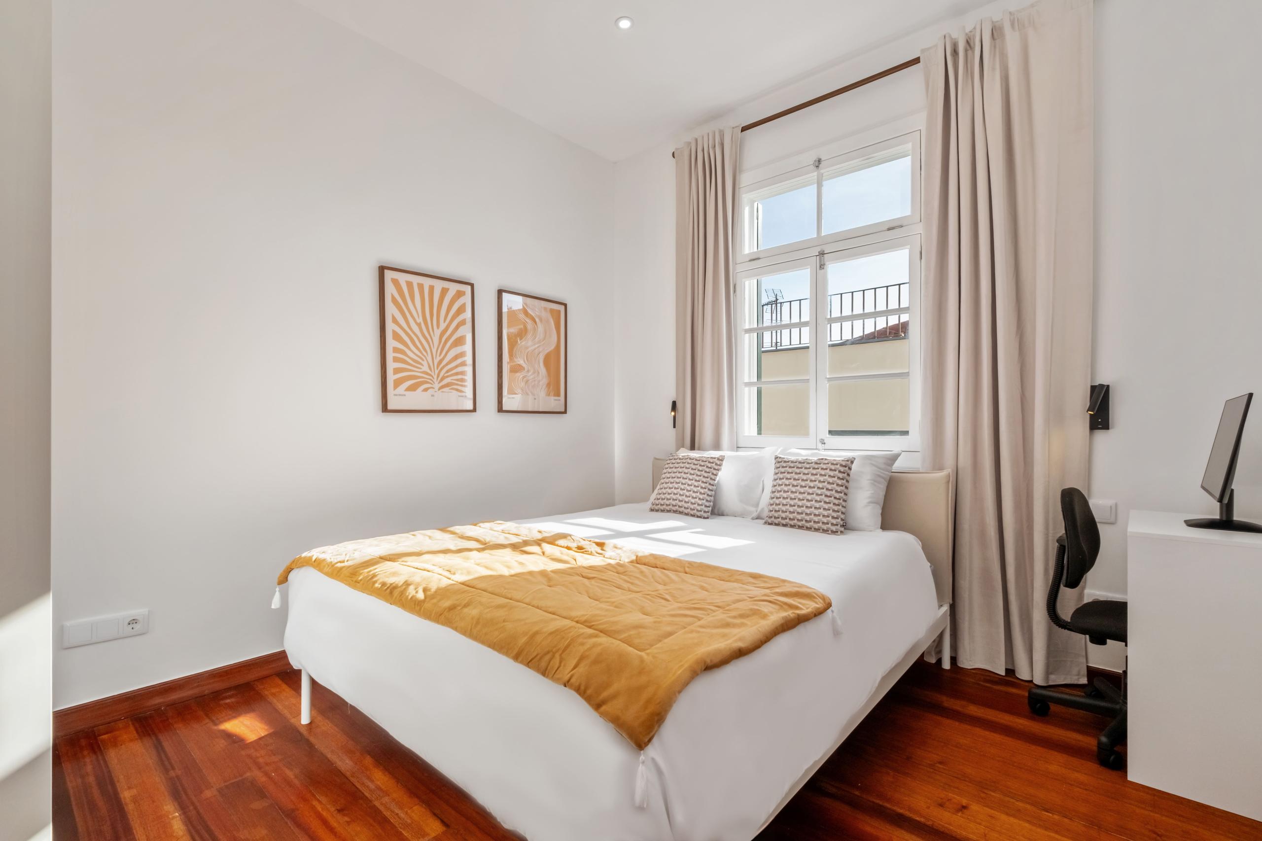 Protea room showing queen bed with orange bedding, artwork, desk with monitor, and wooden floors