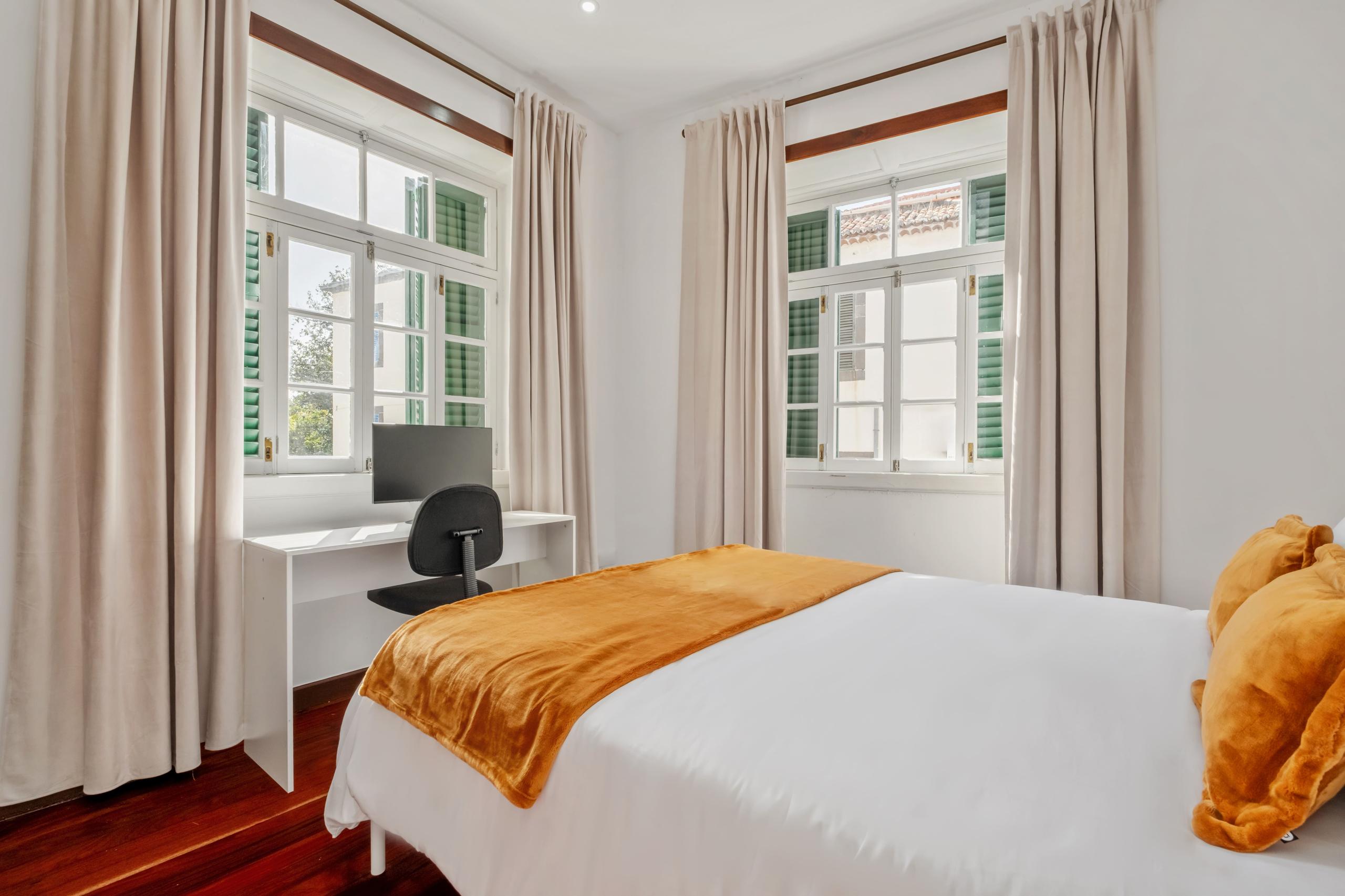 Strelitzia room wide angle showing queen bed, two windows with curtains, and desk area