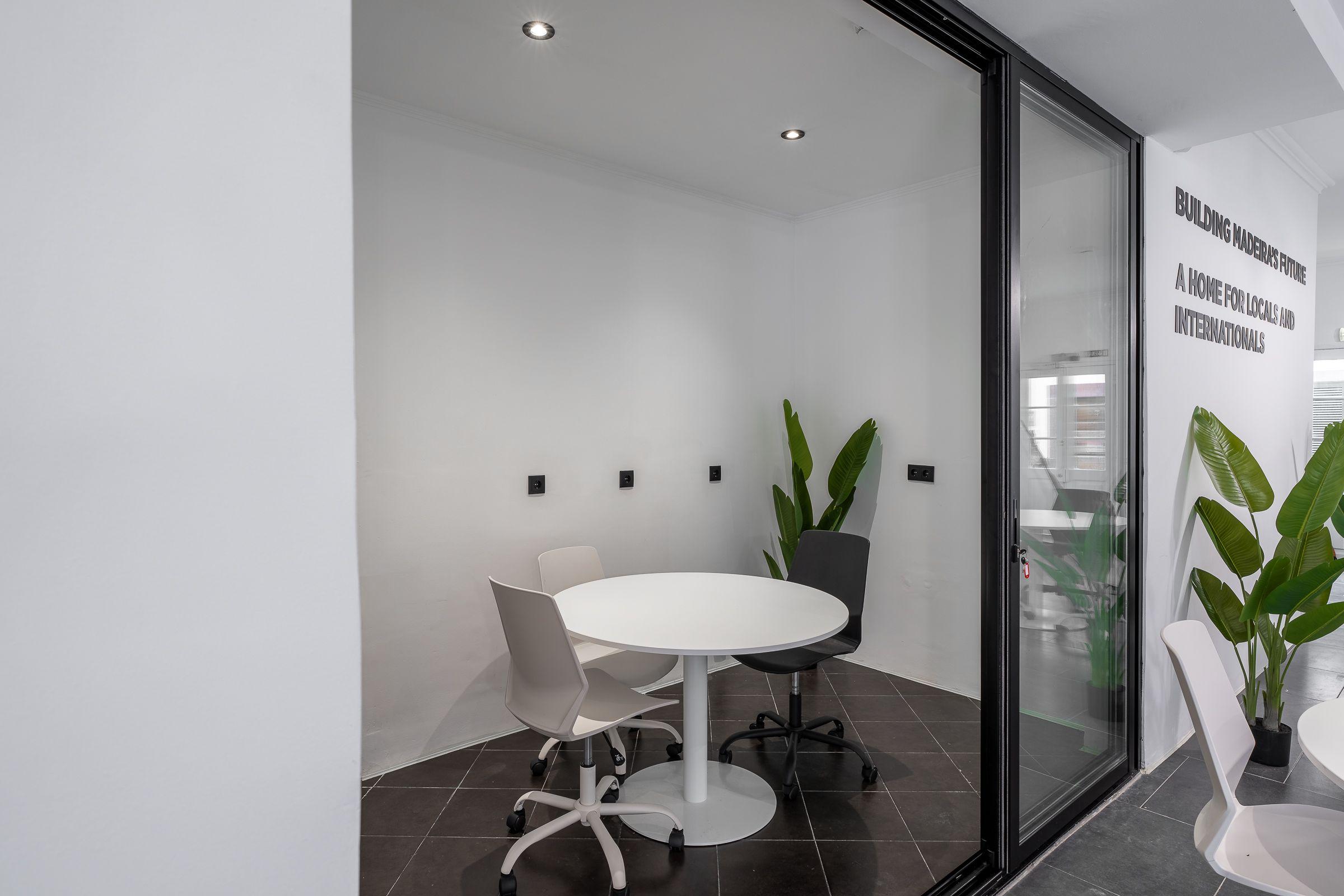 Small glass-walled meeting room with round white table and chairs at Madeira Friends Hub