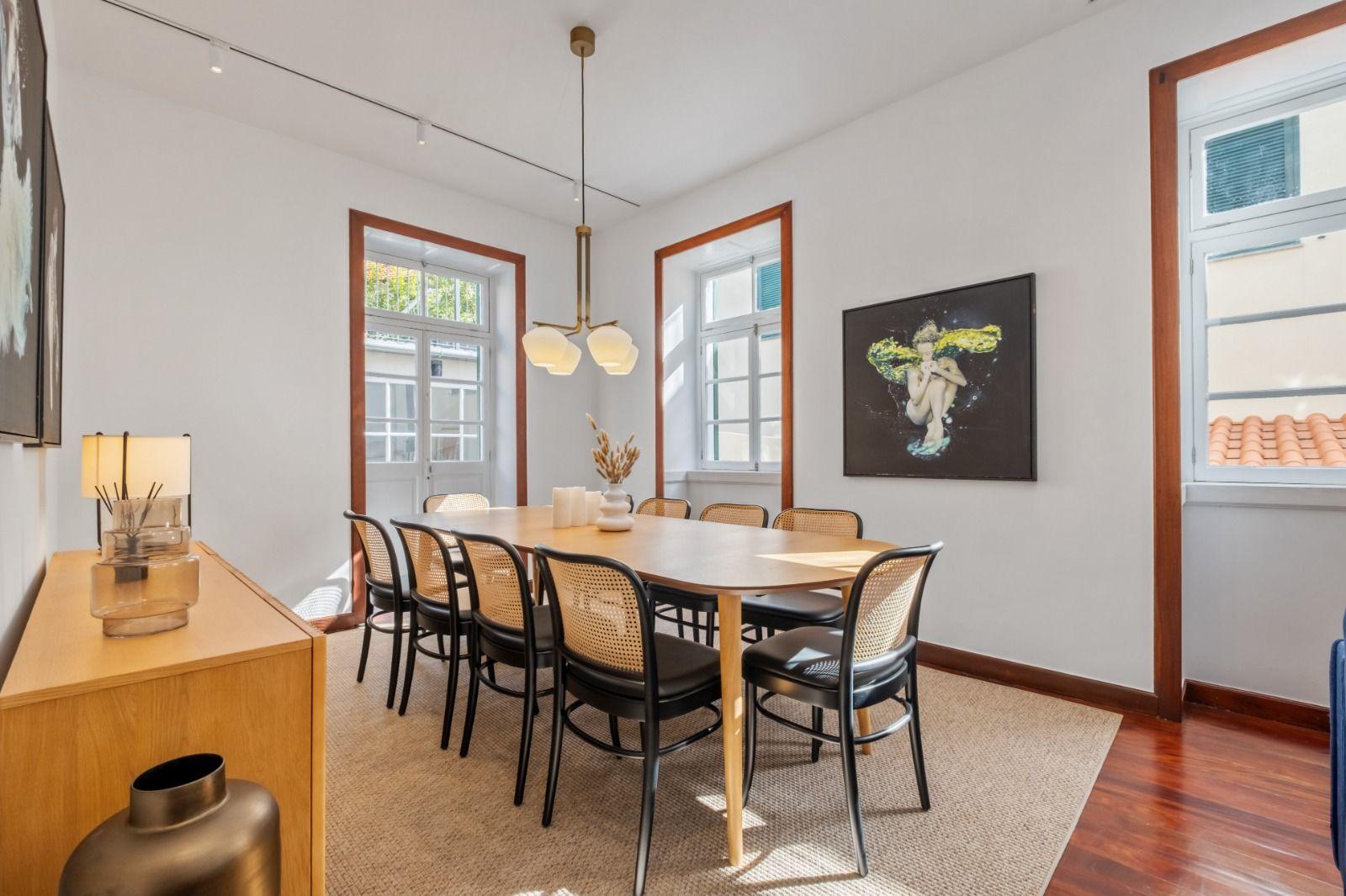 Bright dining room with large wooden table, cane chairs, pendant lighting, and artwork