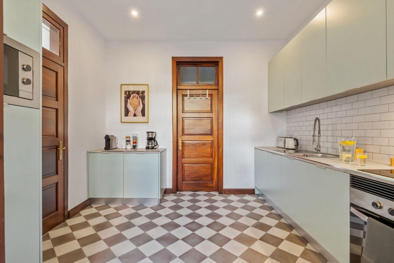 Fully equipped kitchen with checkered tile floor, light green cabinets, coffee machine, and sink