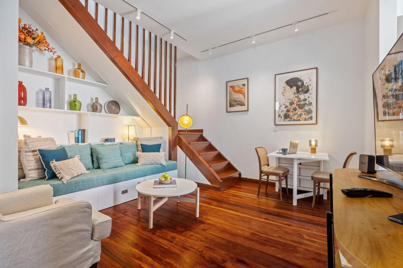 Cozy living room with staircase, built-in shelving, sofa with teal cushions, and wooden floors