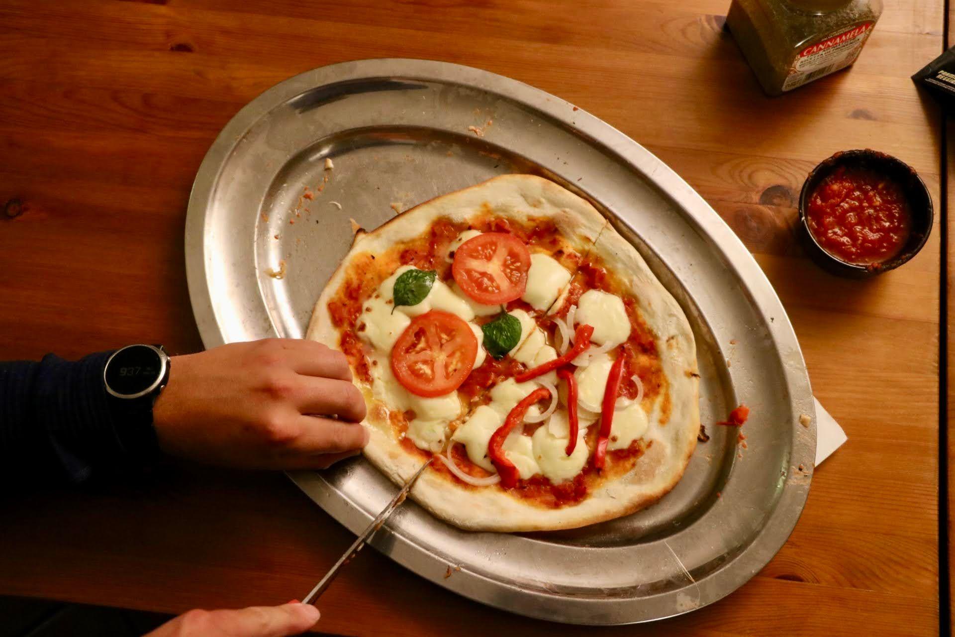 Close-up of a homemade pizza being prepared with tomatoes, mozzarella, and basil on a metal tray