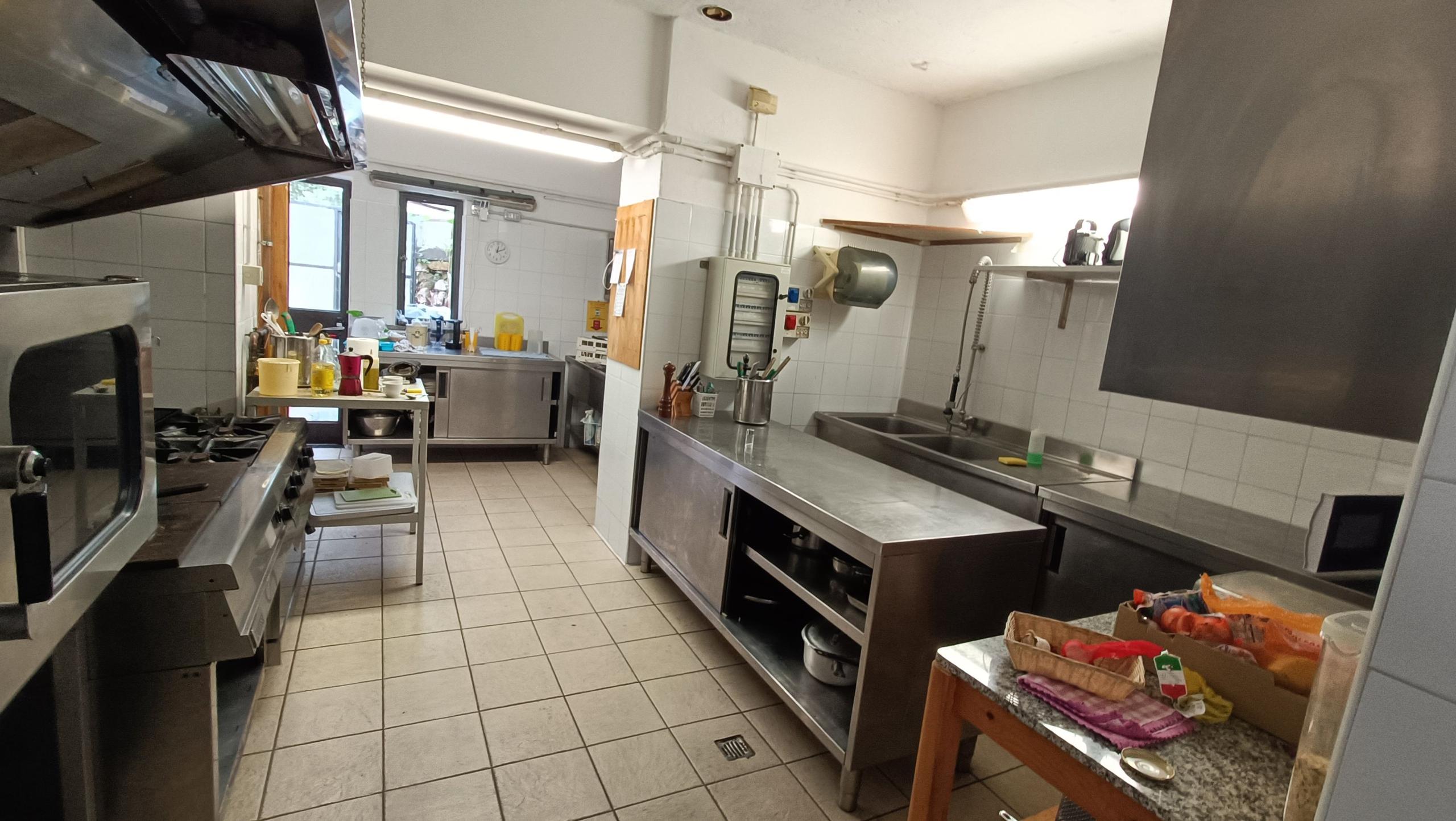 Large professional kitchen with stainless steel counters, industrial equipment, and storage areas