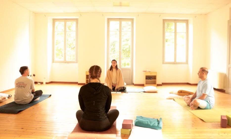 Group yoga or meditation session in the large studio space, with a facilitator leading participants seated on mats