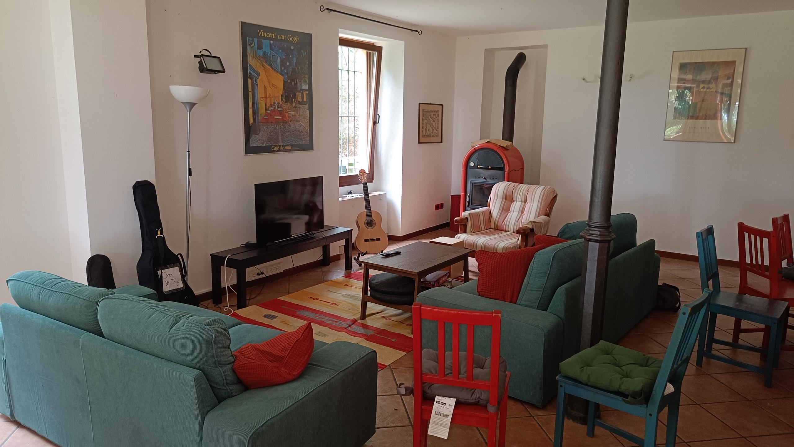 Living room with green sofas, wood-burning stove, TV, guitar, and colorful chairs
