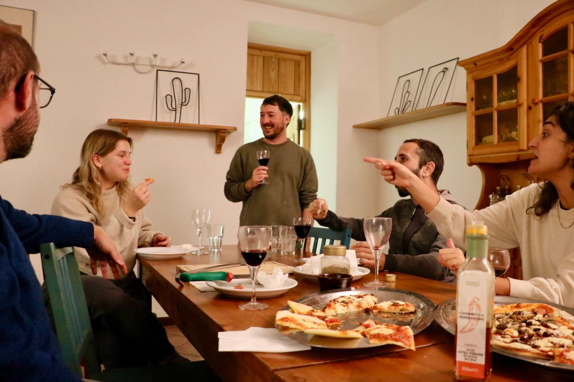 Residents sharing a communal dinner with pizza and wine around a wooden dining table