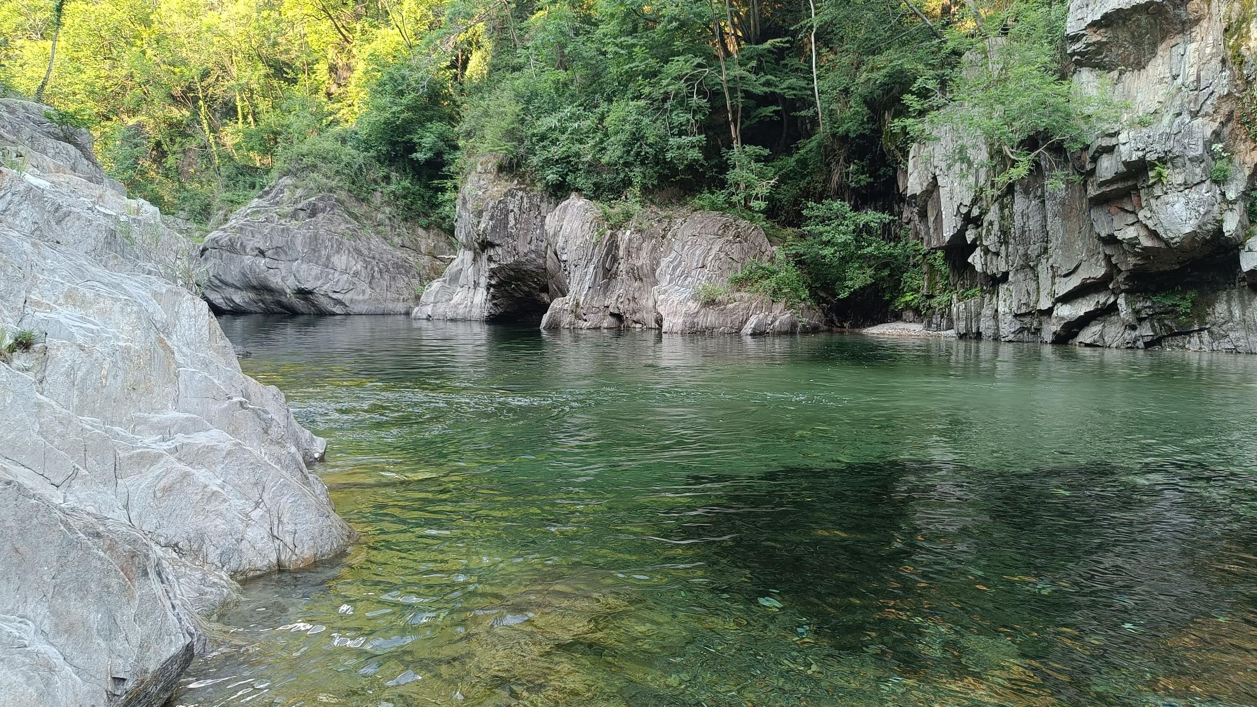 Clear green river with rocky cliffs and lush forest — a natural swimming spot near Montino