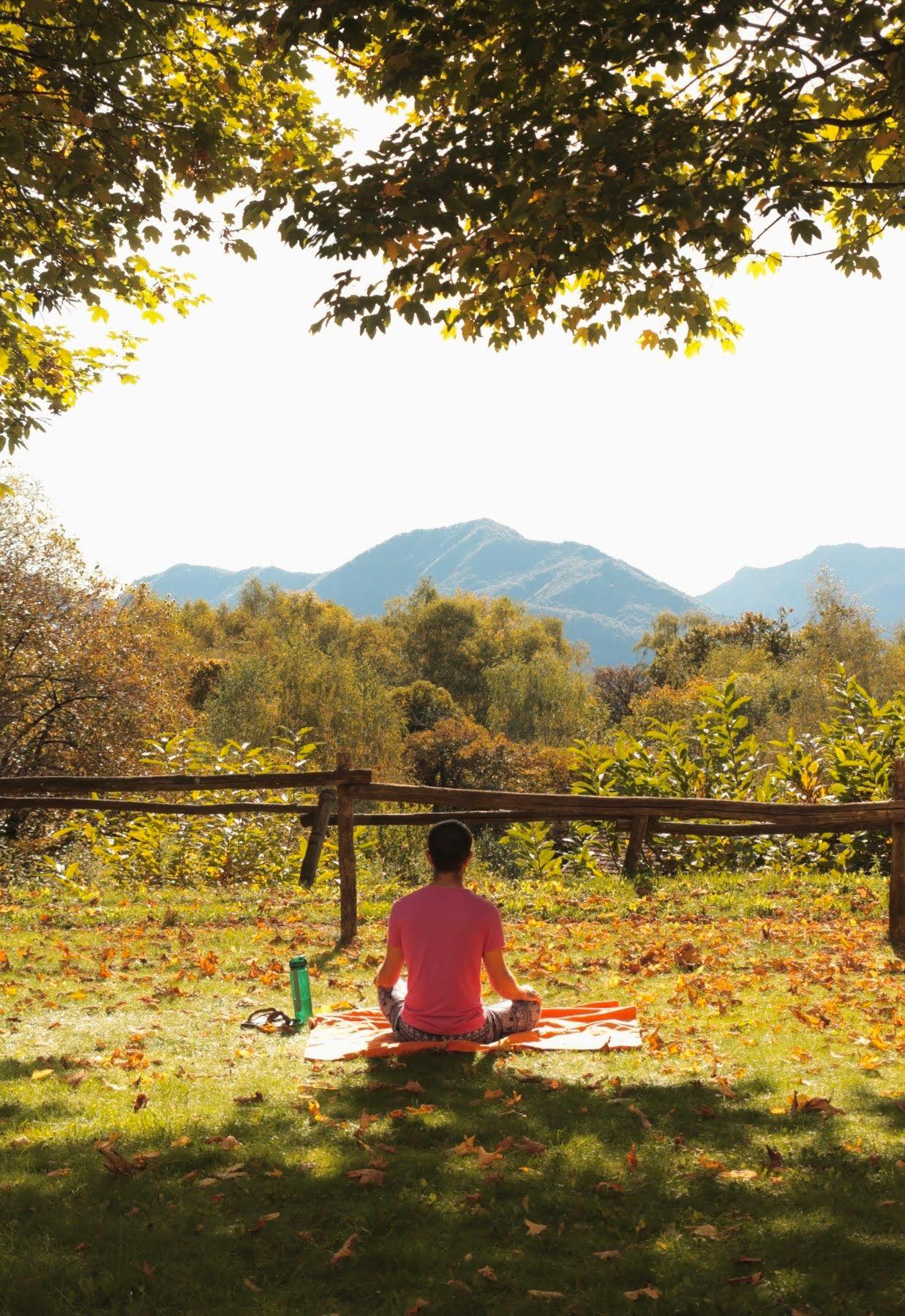 Person meditating in the garden with mountain views in the background, surrounded by autumn foliage