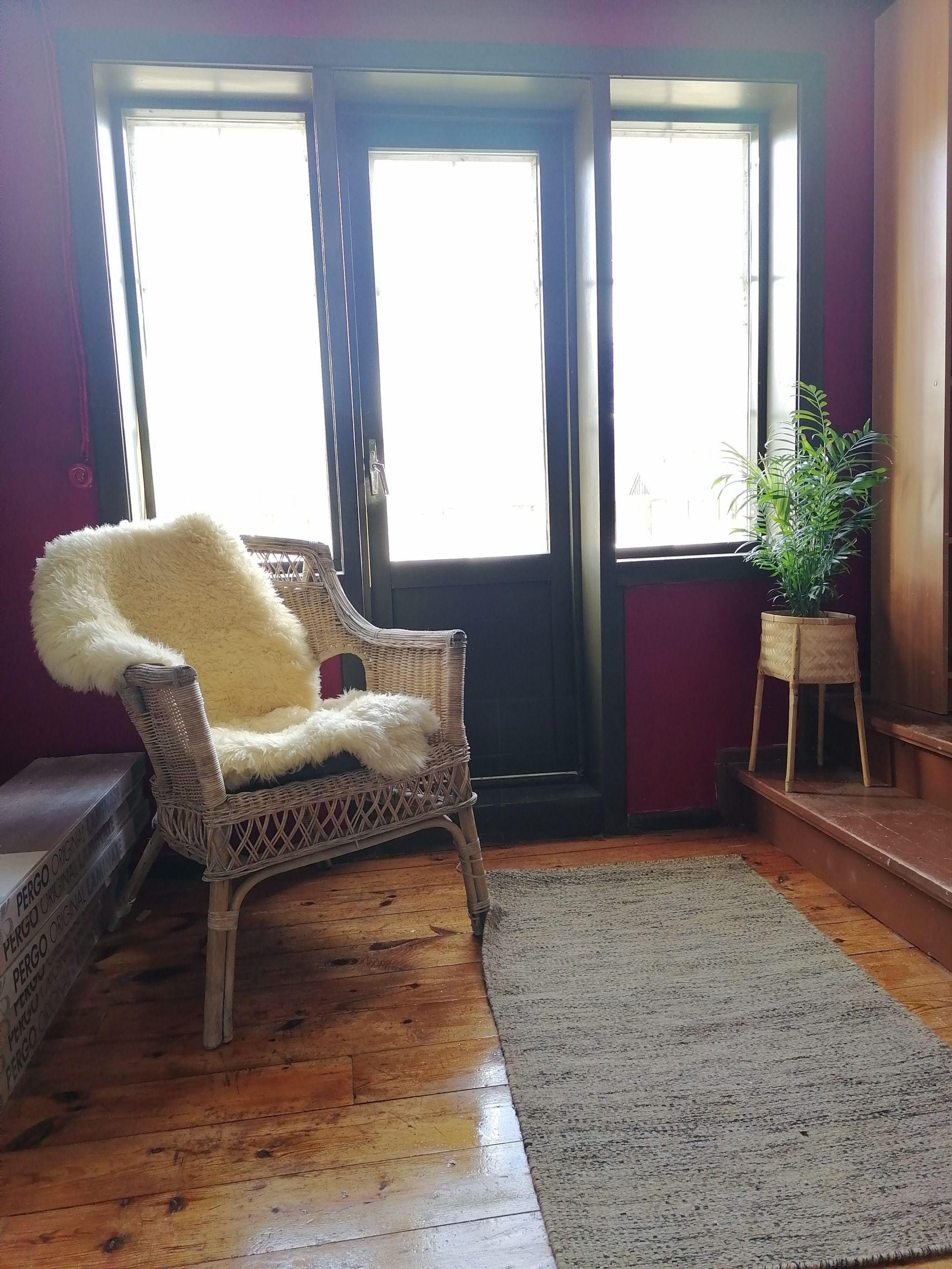 A cosy lounge corner with a wicker chair, sheepskin throw, and plants by the window