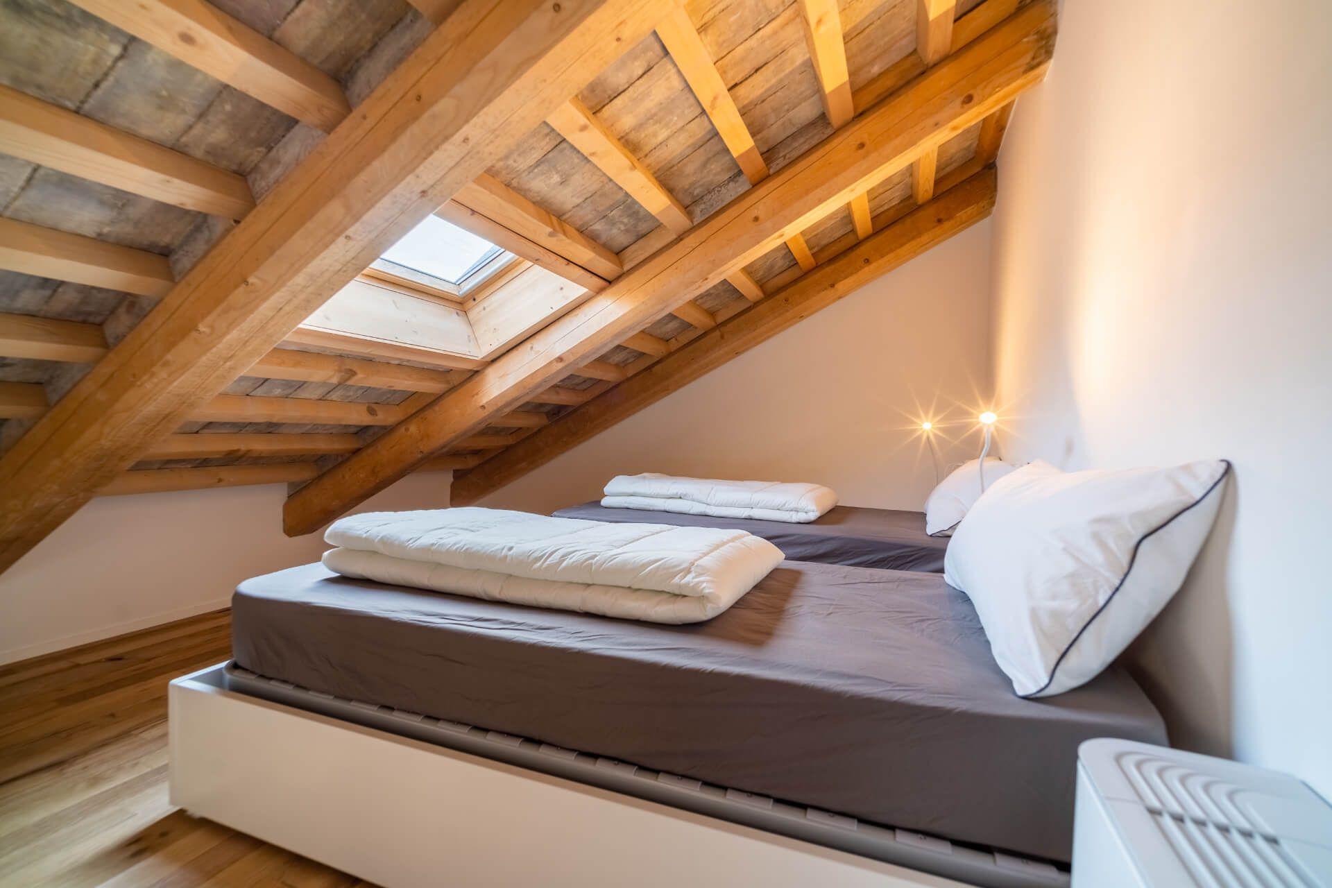 Loft bedroom with a double bed under a sloped wooden beam ceiling with a skylight window
