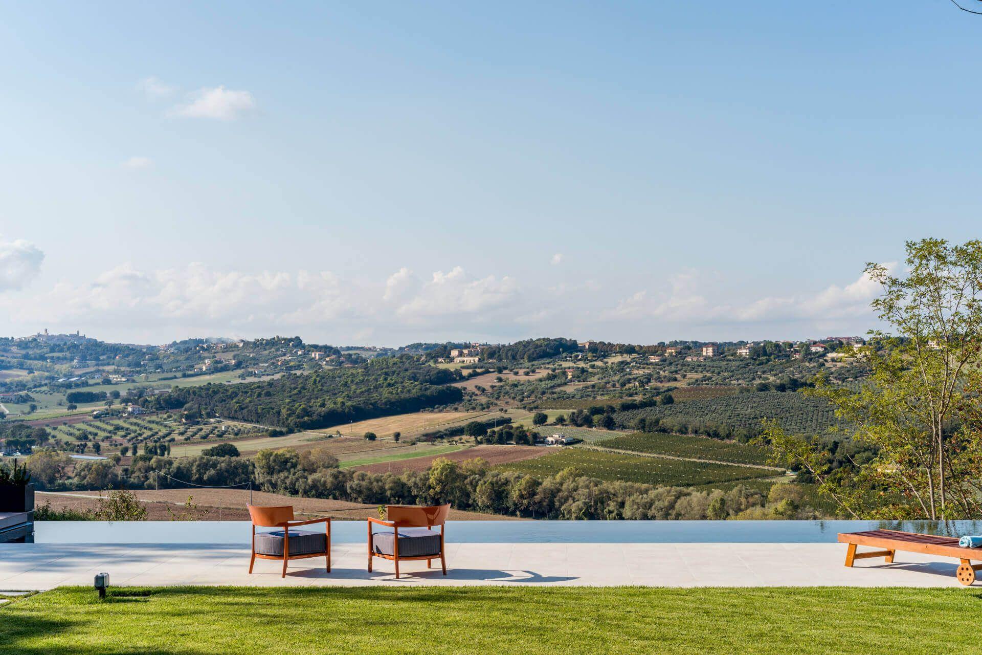 Outdoor terrace with two armchairs beside the infinity pool, overlooking the Marche countryside hills