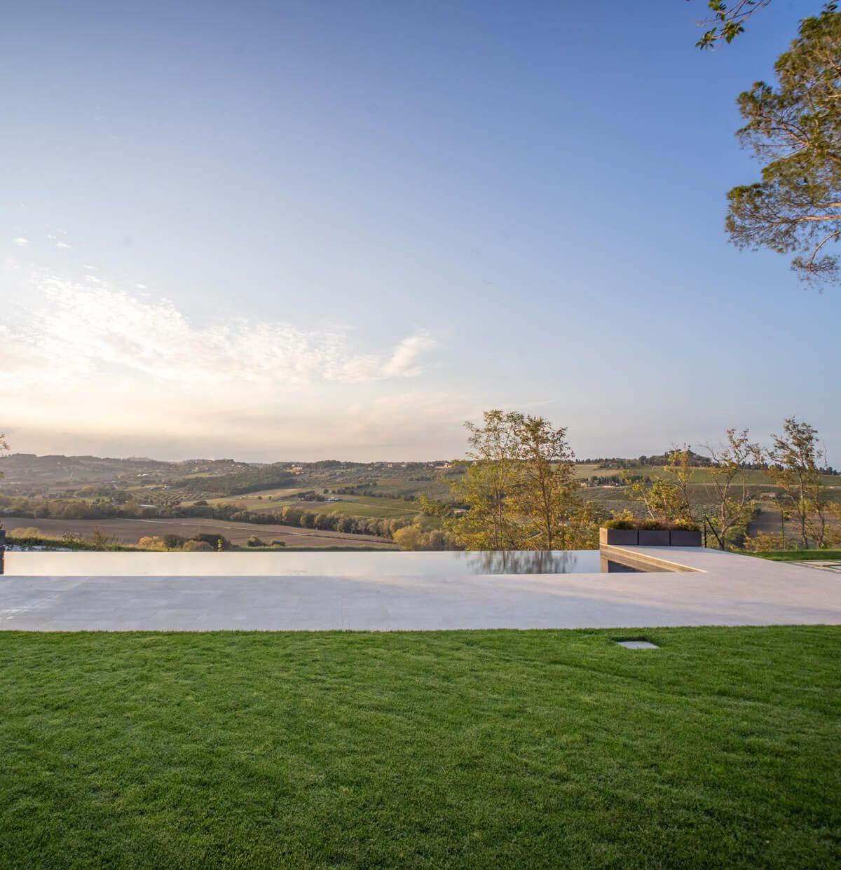 Infinity pool terrace with two armchairs overlooking the rolling Marche hillside at sunset