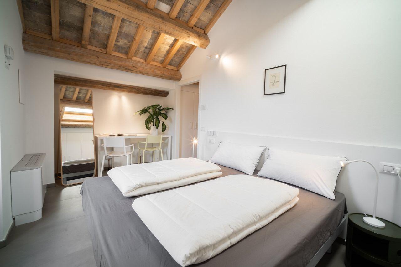 Private smart double room with wooden beam ceiling, bed, and a view into a small dining area