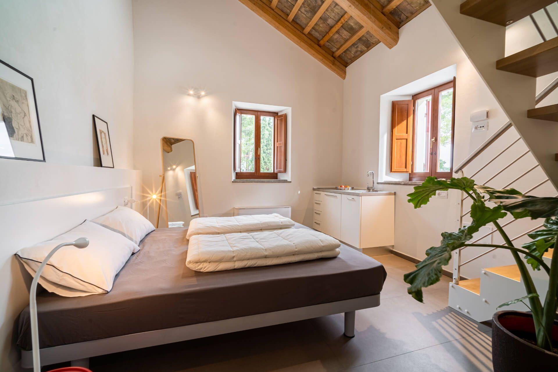 Private double bedroom with wooden beam ceiling, kitchenette, and a loft accessible by stairs
