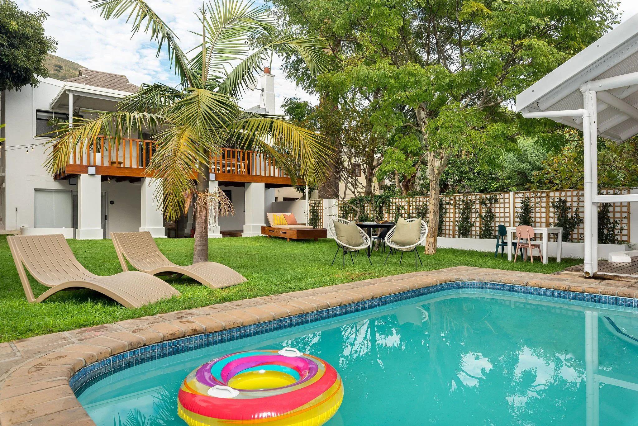Sparkling outdoor swimming pool at Neighbourgood Hill with sun loungers, palm trees, lush green garden, and a colourful pool float