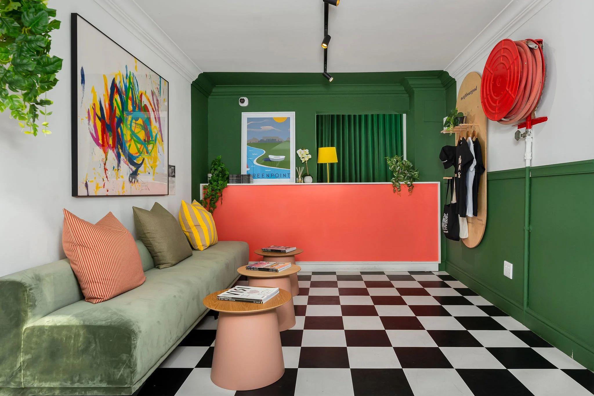 Colourful reception and lounge area at Neighbourgood Hill with green walls, checkered floor, green velvet sofa, and reception desk
