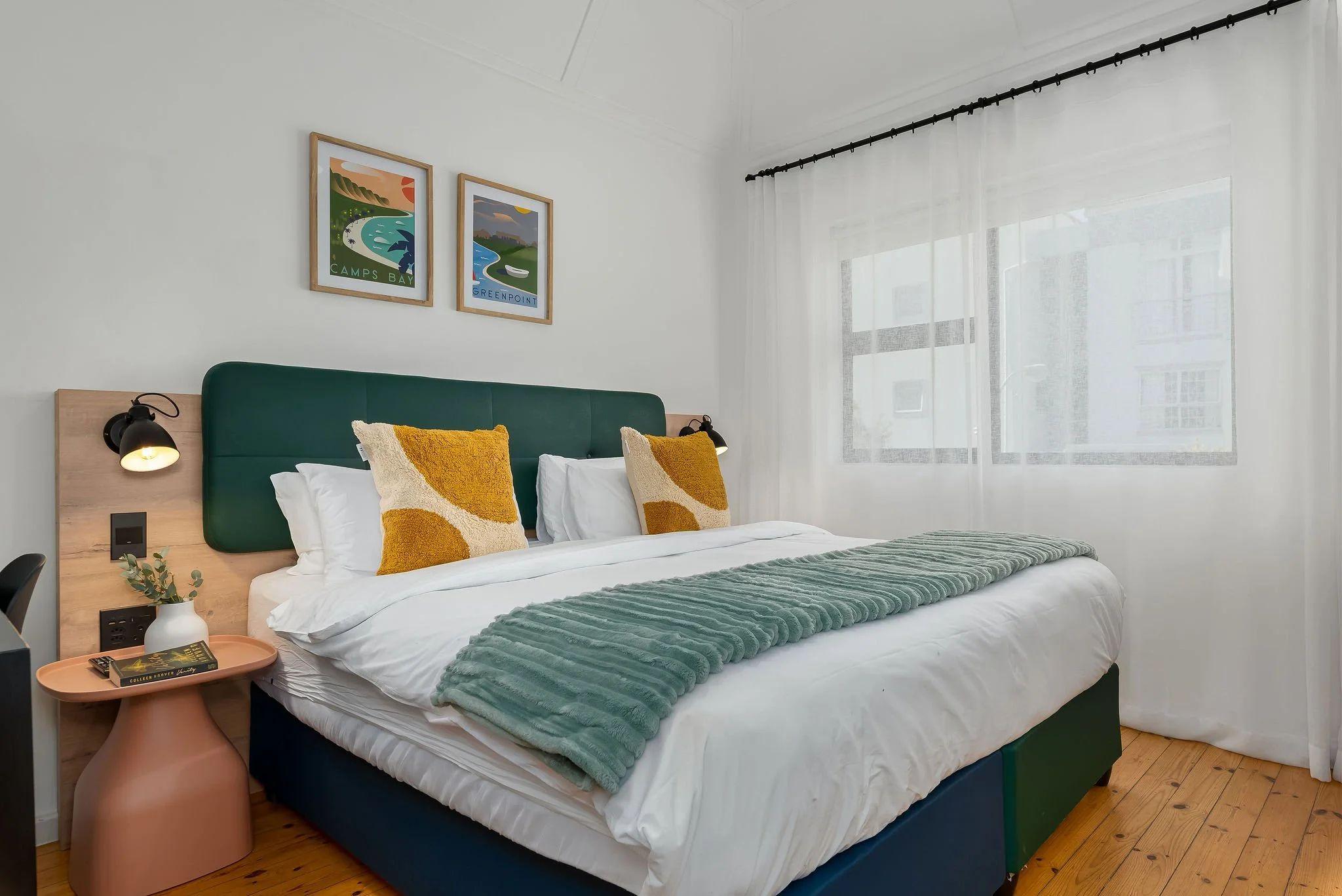 Standard room at Neighbourgood Hill with queen-size bed, green headboard, work desk, and travel posters