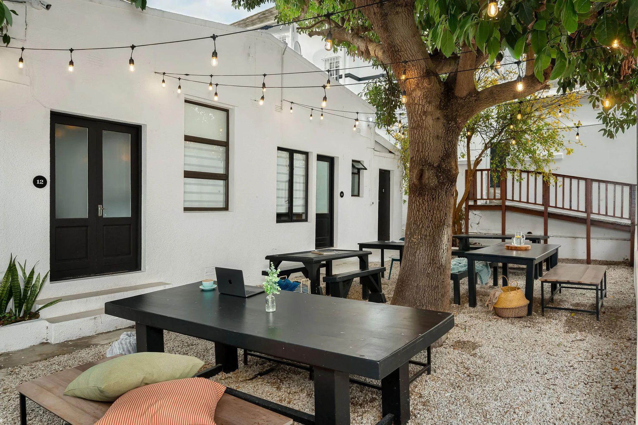 Garden courtyard at Neighbourgood Hill with outdoor picnic tables under string lights and a large tree, laptop on table