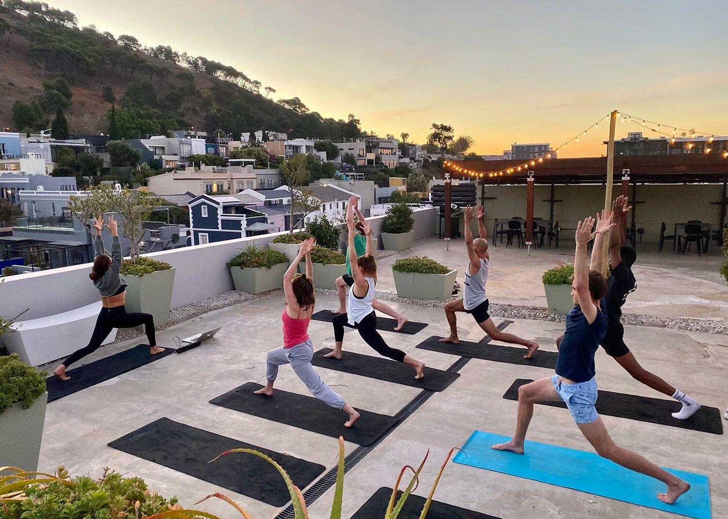 Group yoga session on a rooftop terrace at sunset, with Cape Town neighbourhood and hills in the background
