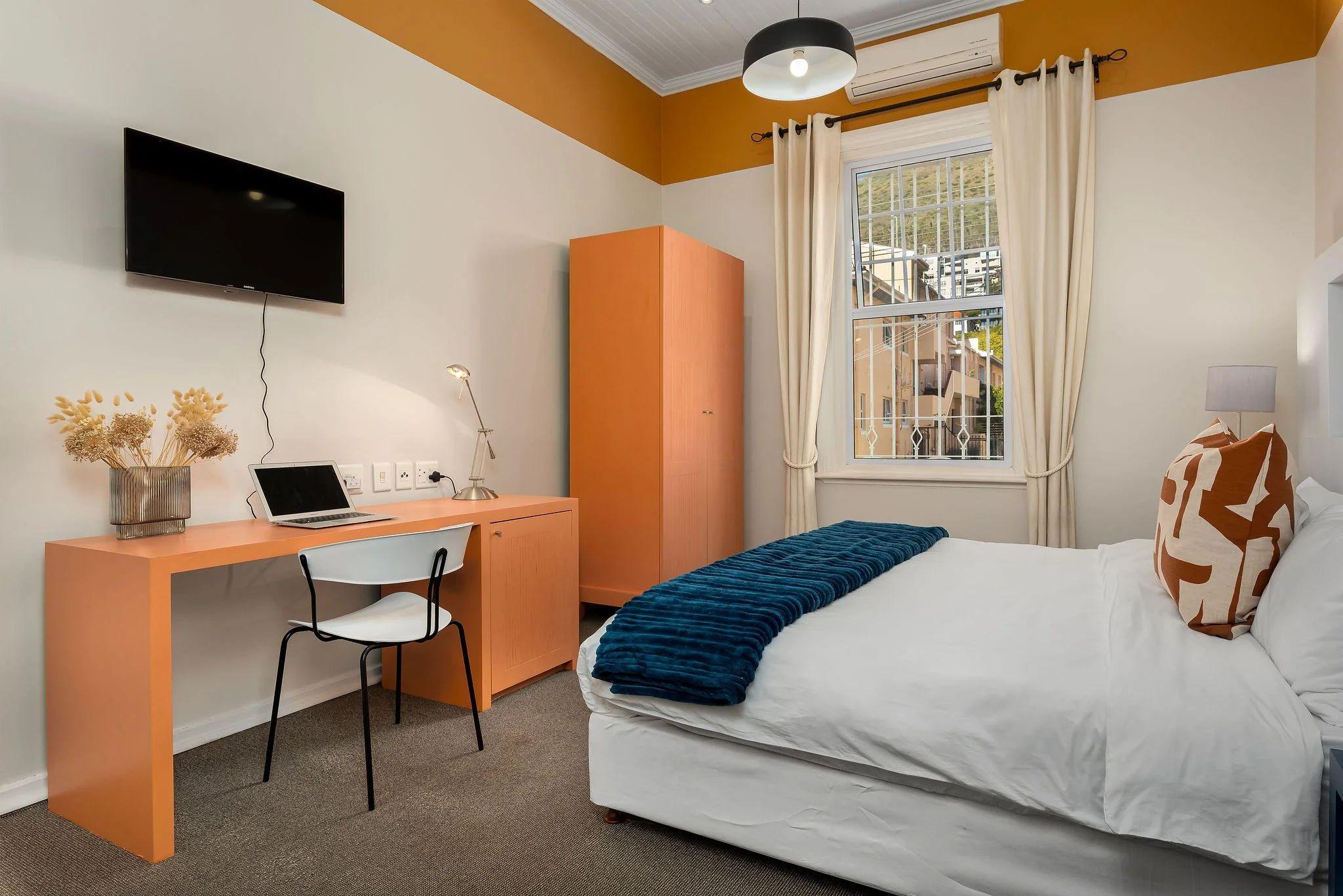 Hill Suites Deluxe room with king-size bed, orange desk and wardrobe, flat-screen TV, and large window