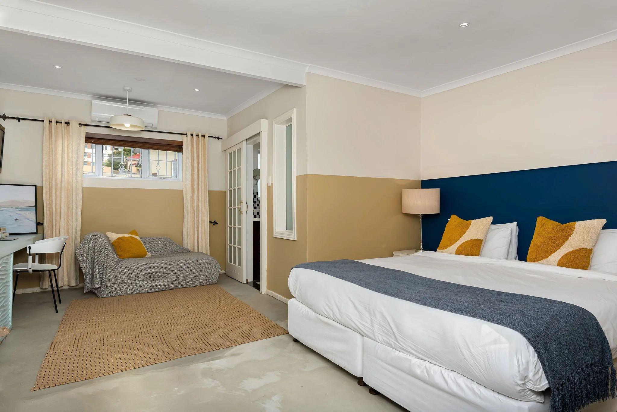 Hill Suites Standard room with king-size bed, blue accent wall, yellow cushions, and work desk