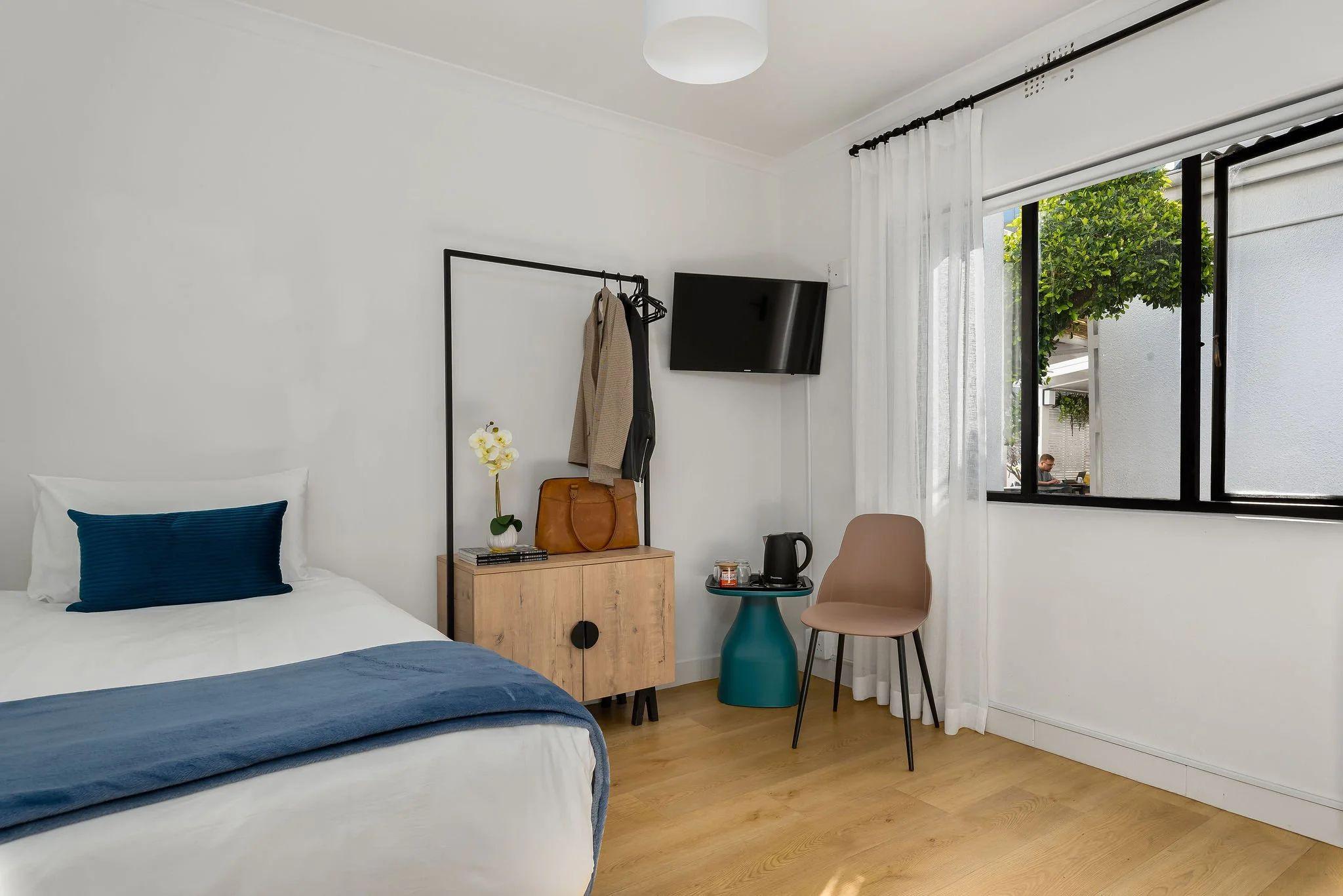 Economy single room at Neighbourgood Hill with single bed, open wardrobe rack, flat-screen TV, and window overlooking the garden