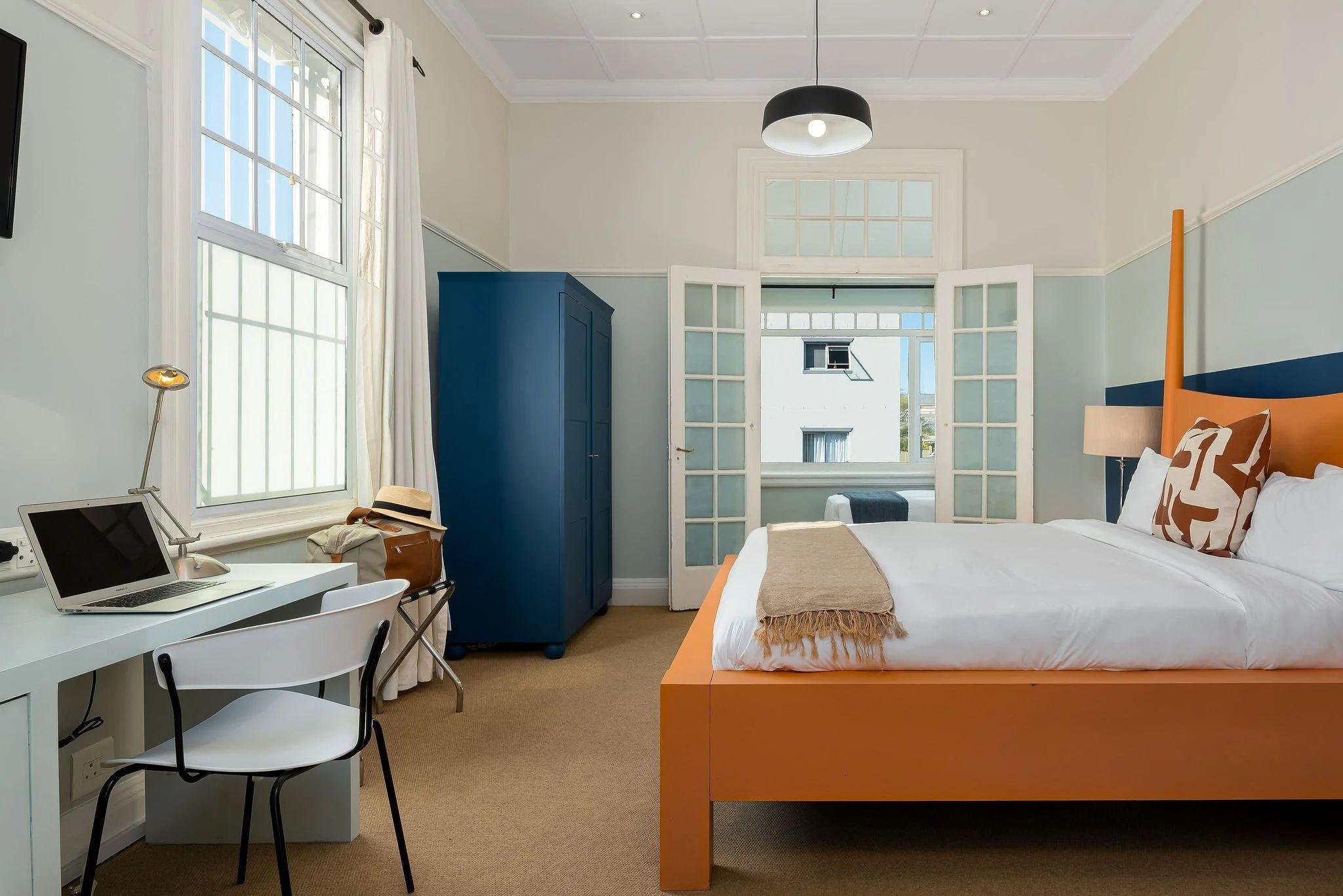 Spacious Hill Suites Deluxe room with king-sized orange bed frame, work desk, blue wardrobe, and large windows